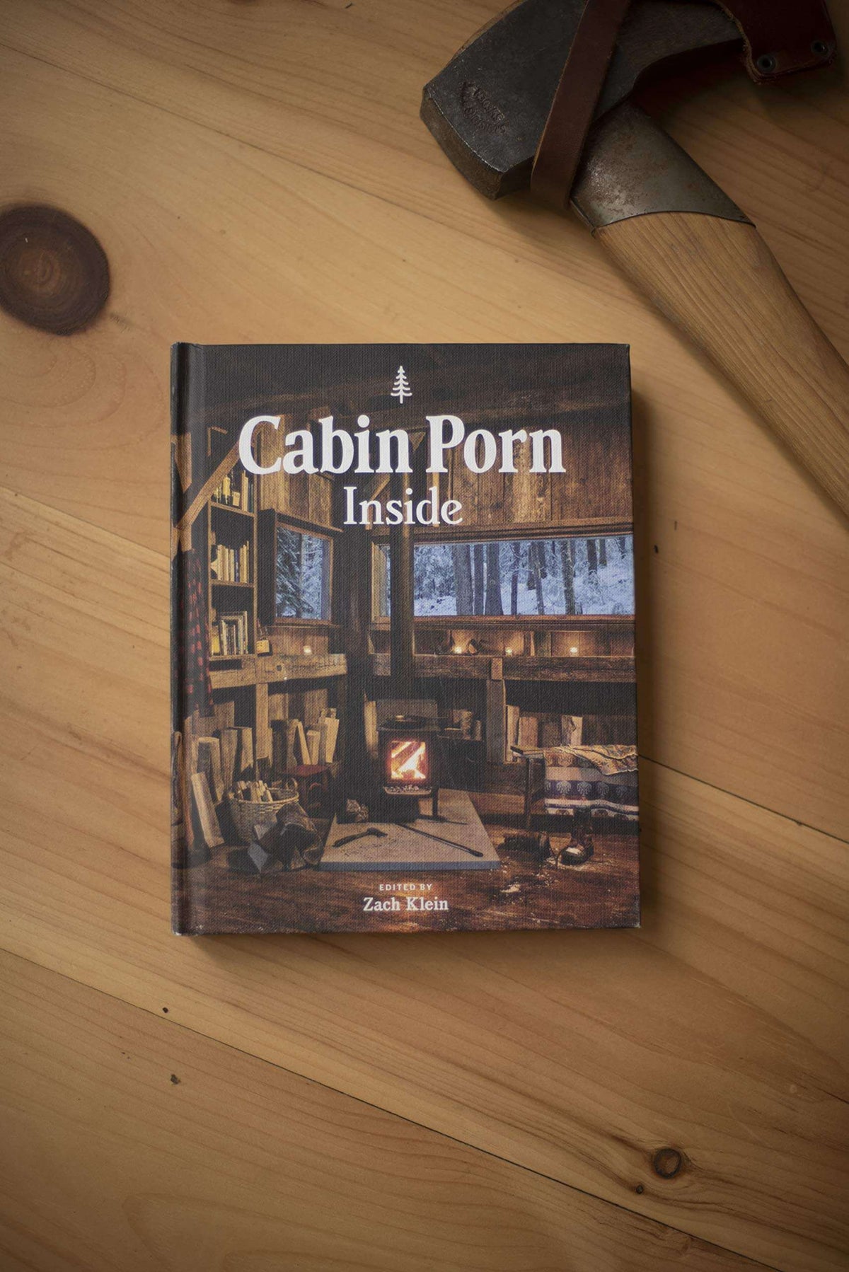 "Cabin Porn Inside Book" on wooden floor, showcasing tranquil cabin interiors, available at Cabin Depot for rustic inspiration.