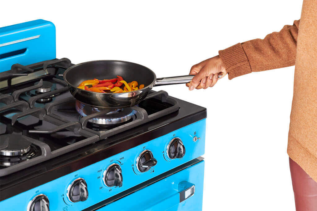 Person cooking on Unique Classic Retro 30" Convection Gas Range from Cabin Depot, featuring iconic 1950s design and blue chrome accents.