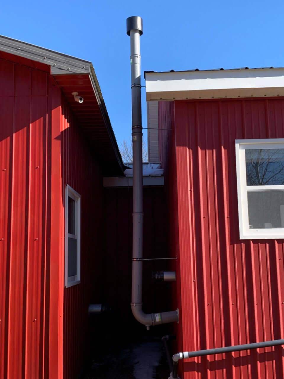 Cinderella 4" x 36" flue pipe installed between red buildings, part of Cabin Depot's collection for efficient flue ventilation solutions.
