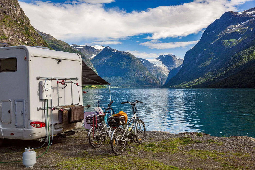 Riverside view with camper, bicycles, and mountainous landscape, depicting outdoor adventure and travel.