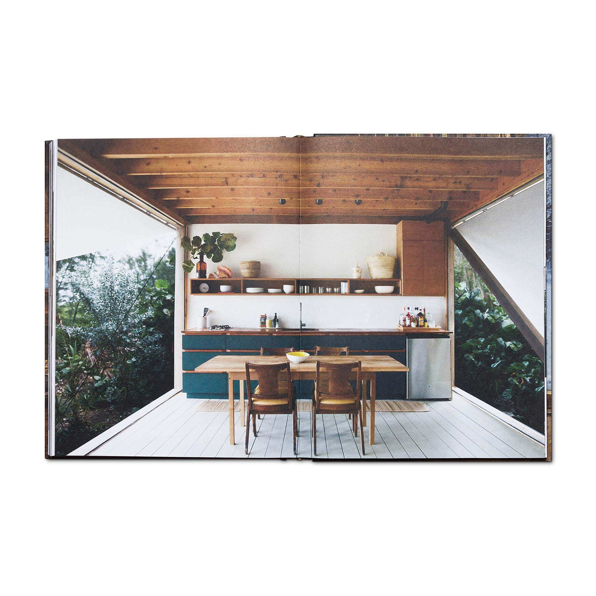 Open book showing a modern cabin interior with wooden beams, dining table, and greenery; from Cabin Porn Inside, available at Cabin Depot.